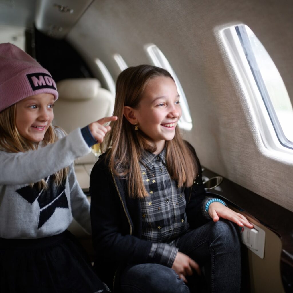 Two sisters sitting inside private jet airplane and looking outside the window.